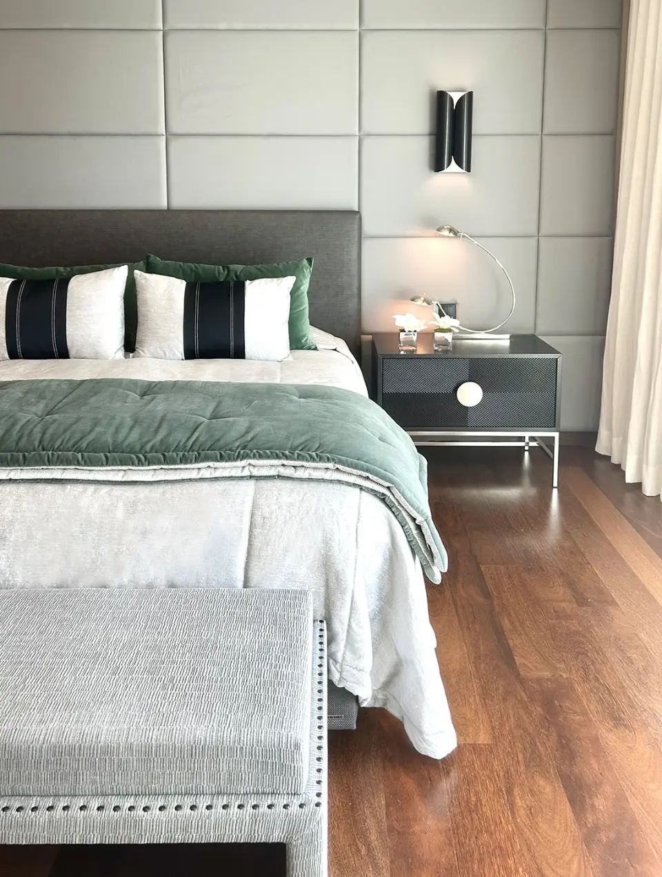 The suite is decorated in shades of green and gray, featuring an upholstered headboard panel, a gray fabric headboard, and a custom-designed nightstan